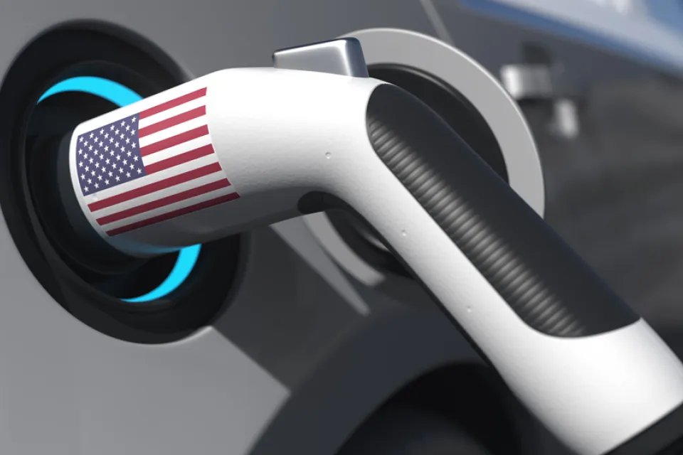 An electric vehicle charger with an American flag sticker is shown plugged into a car.
